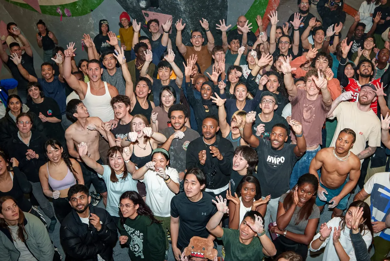 Large group of people with hands raised, celebrating together indoors at a climbing wall venue.