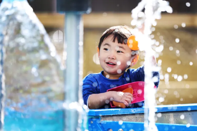 Young child playing with water and a red cup at an interactive water play exhibit.