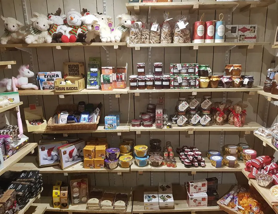 Shelving unit displaying farm shop merchandise including stuffed animals, jars of preserves, packaged foods, and gift items.