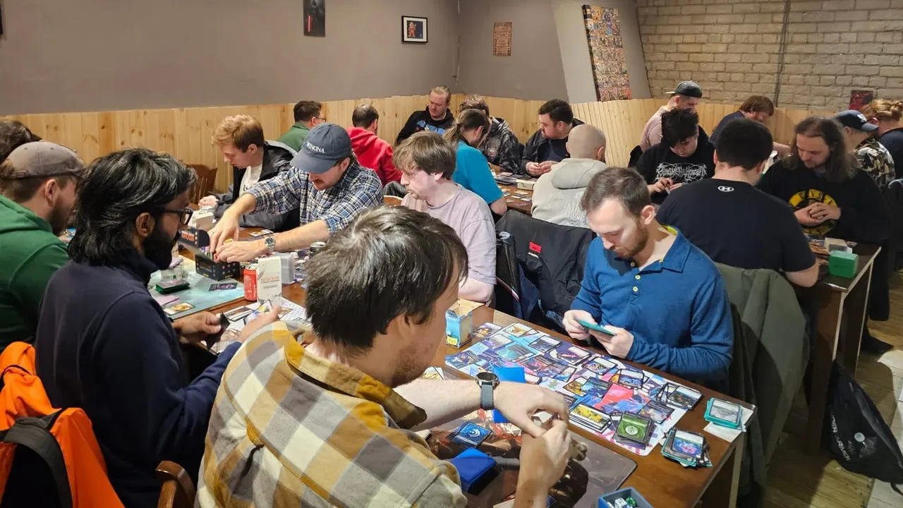 Group of people seated at tables playing trading card games in a community hall.