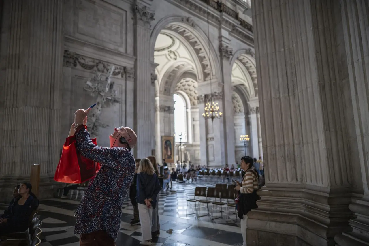 An adult holding up a young child wearing a red cape inside a grand cathedral with soaring arched columns and ornate stonework.