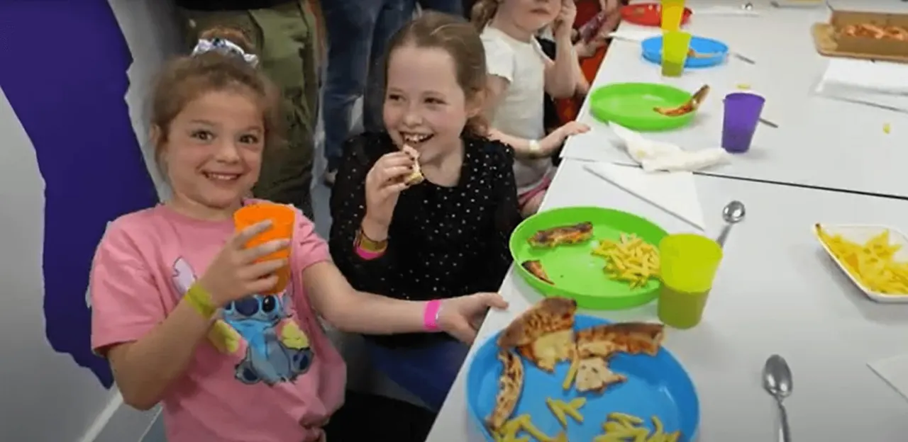 Children enjoying a meal together at a table with colourful plates and cups during an indoor play session.