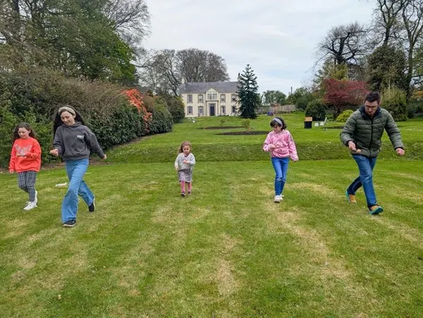 Children and adults running across a grass lawn with a historic house visible in the background.