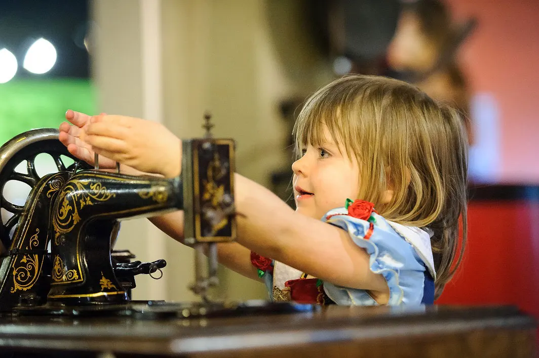 Young child operating an ornate vintage sewing machine on display at a museum.