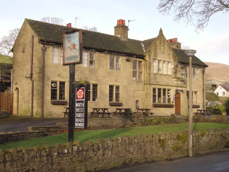 Stone country pub with picnic tables outside, bare winter trees and moorland hills in background.
