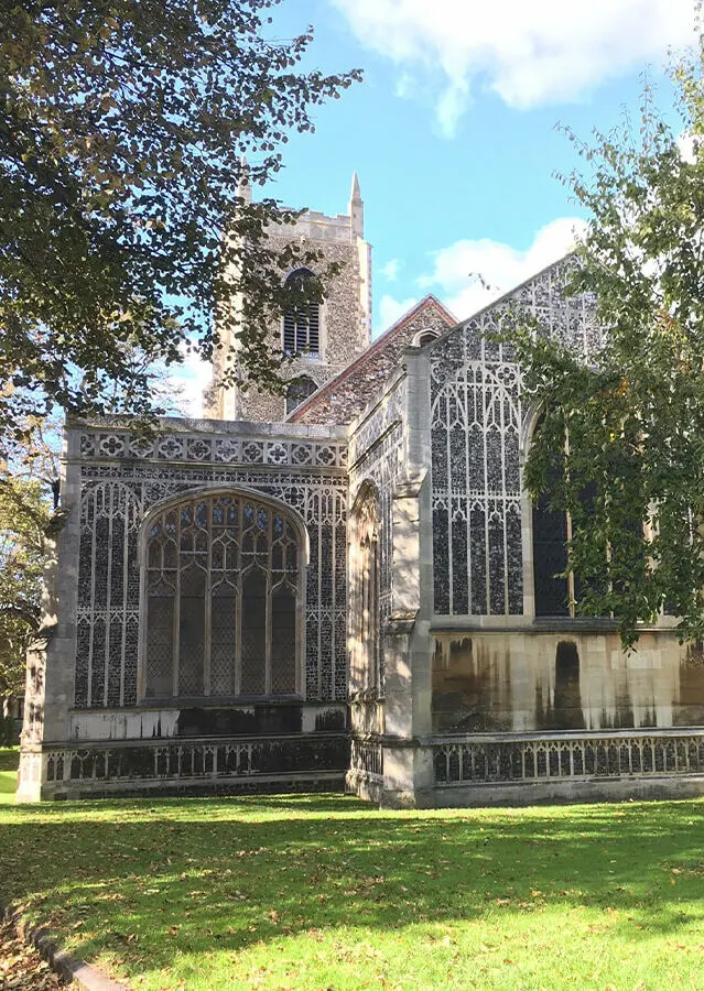 Historic stone church with ornate Gothic windows and spire, surrounded by trees and green lawn.