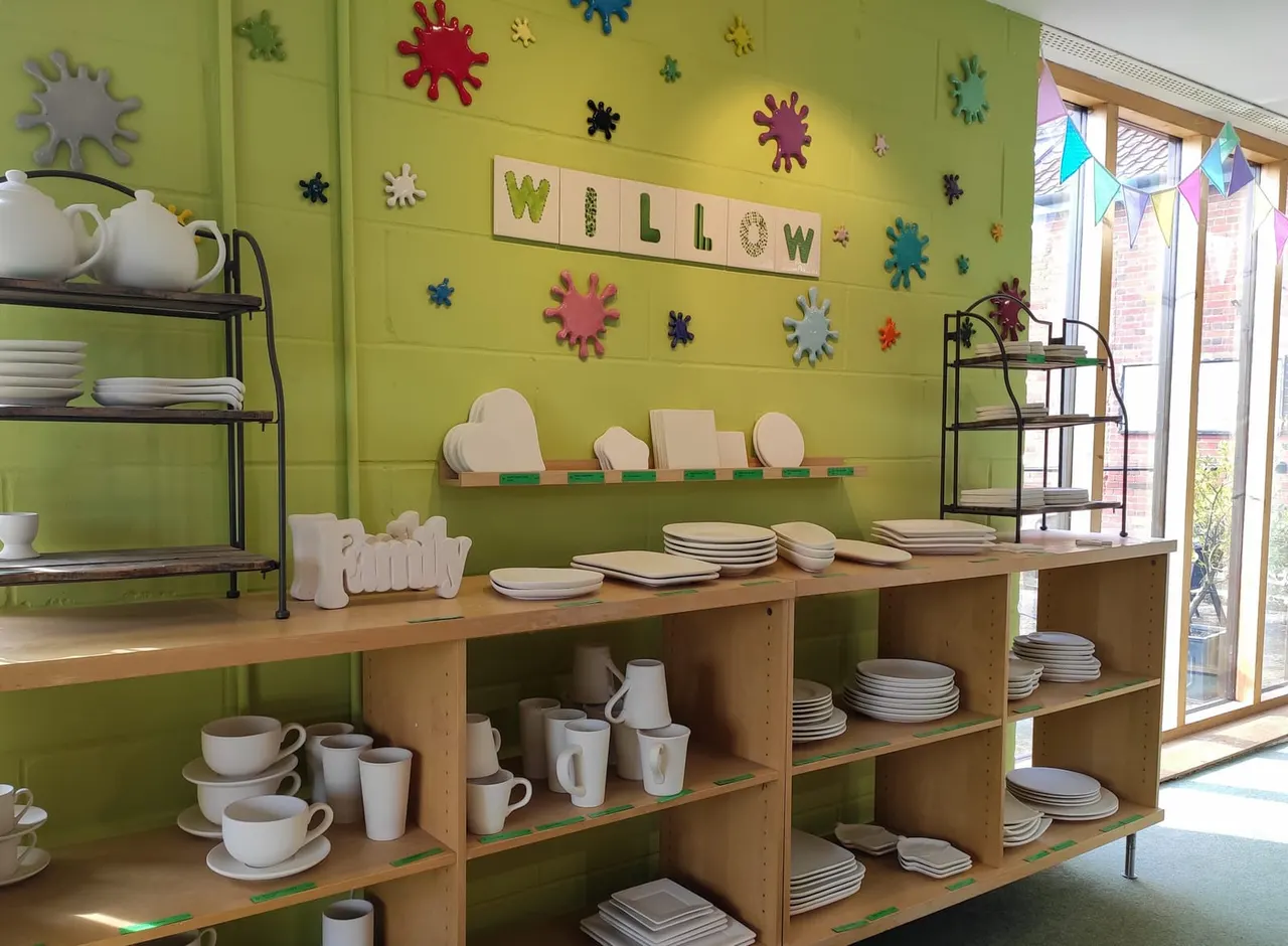 A bright green room displays tableware and crockery on wooden shelves and units, with colourful foam shapes and bunting decorating the walls.