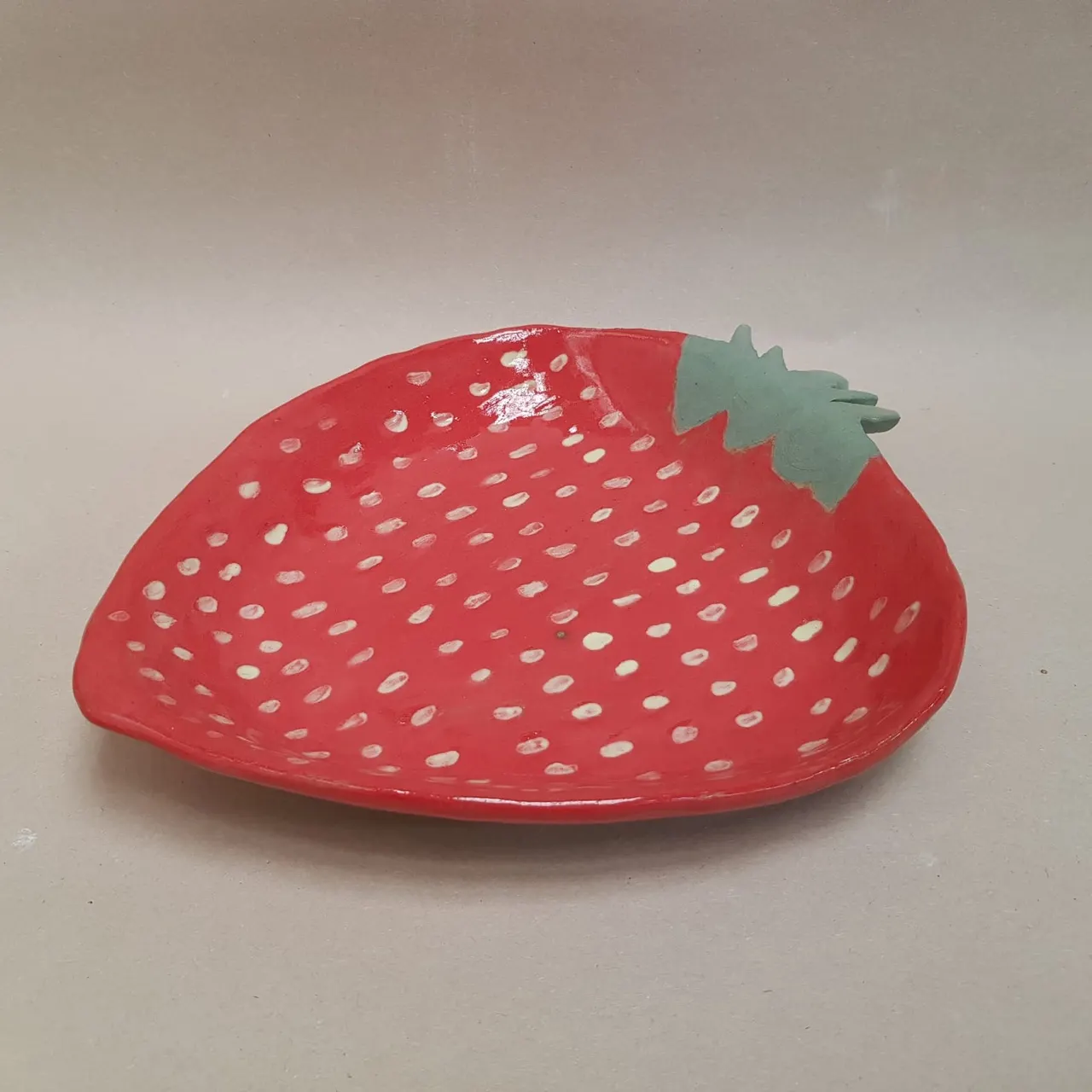 Red strawberry-shaped ceramic dish with perforated pattern and green leaf detail.