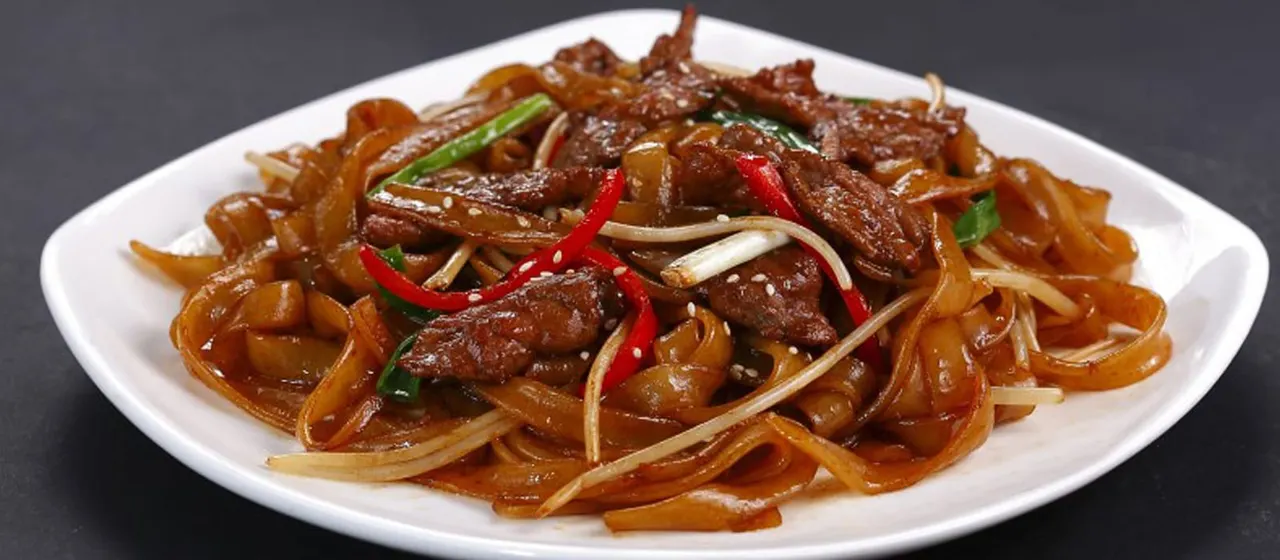Stir-fried beef with noodles, peppers and ginger on a white plate.