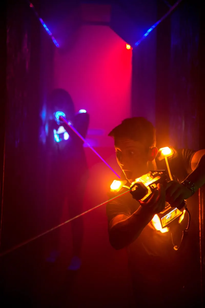 Laser tag players in neon-lit arena holding glowing equipment during gameplay.