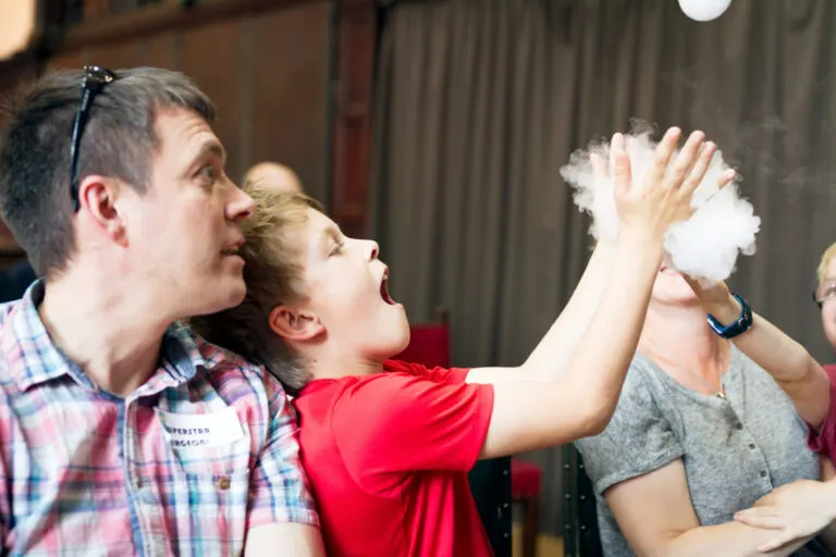Man and child participate in a hands-on science experiment involving white foam or cloud-like substance at an indoor activity centre.