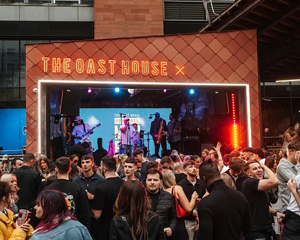 Crowd of people dancing and watching a live band perform on an outdoor stage at night.
