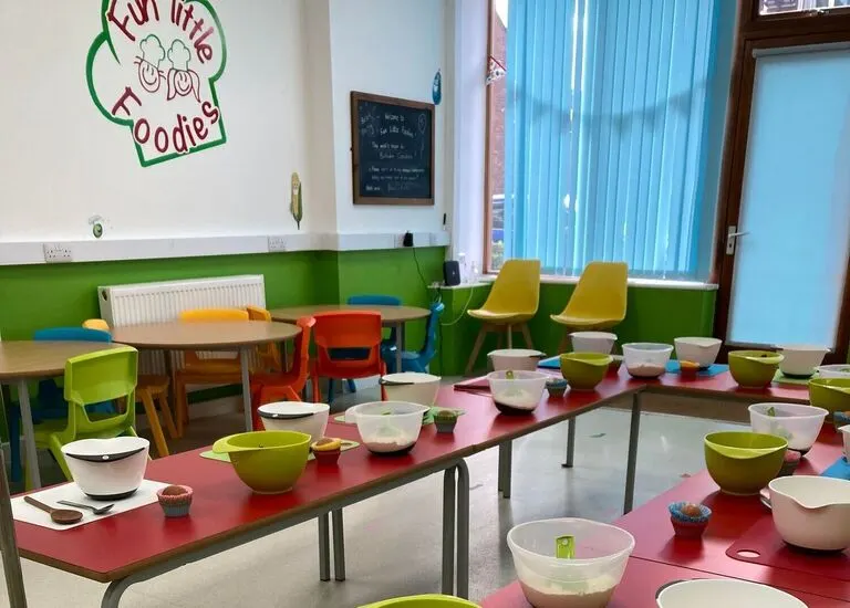 Bright, colourful children's activity room with red and pink tables set with bowls and utensils, green and yellow chairs, and a green-painted wall.