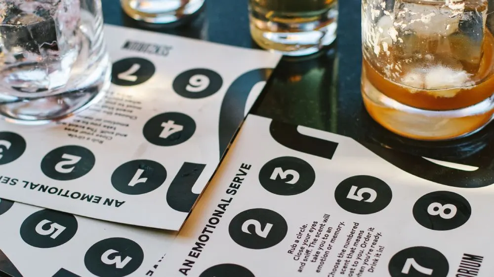 Glasses of whiskey and water beside a numbered tasting guide on a dark table.