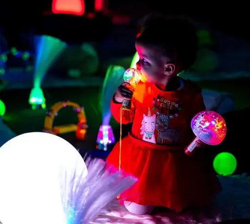 Child playing with glowing toys in a brightly lit interactive play area with neon colours.
