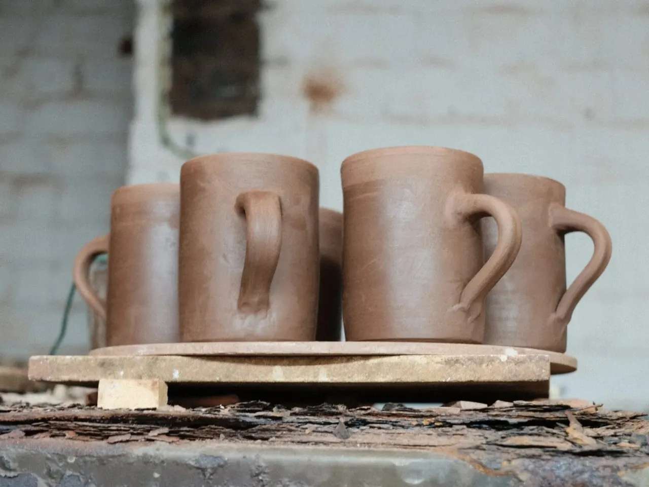 Handmade terracotta mugs and beakers arranged on a wooden base in a pottery studio.