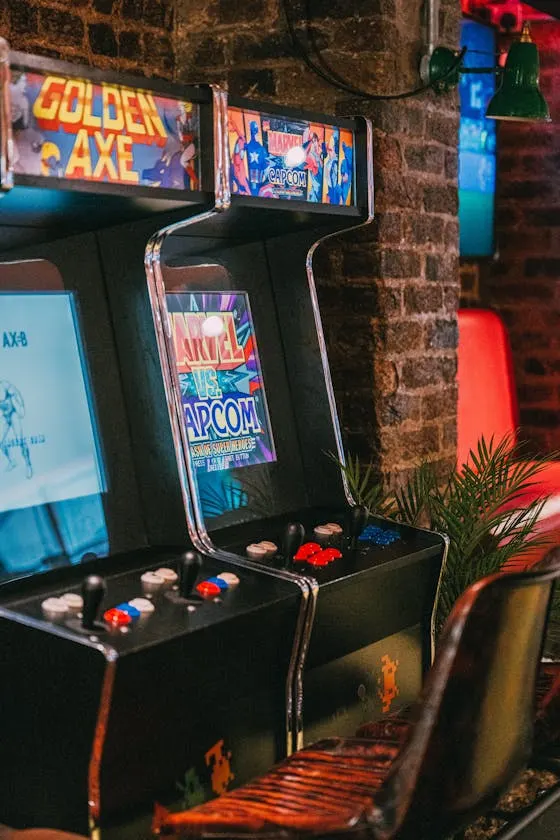 Vintage arcade game machines against a brick wall, lit with neon signs.
