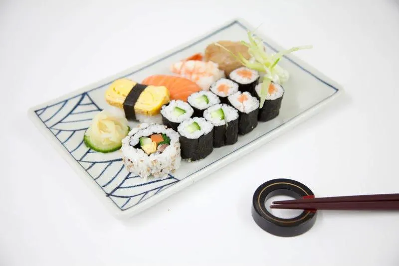 Assorted sushi and nigiri arranged on a decorative plate with chopsticks beside it.