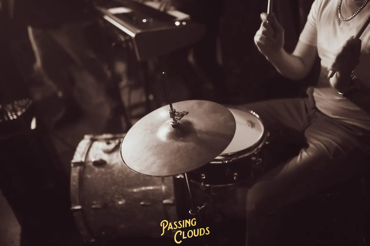 Drummer playing cymbals during a live music performance in a dimly lit venue.