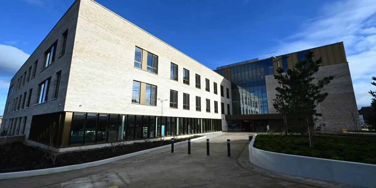 Modern brick and stone library building with curved plaza courtyard and landscaping under blue sky.