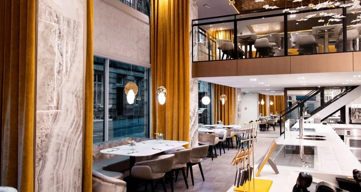 Modern fine dining restaurant interior with marble walls, gold curtains, and tables set for service.