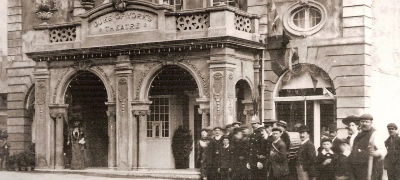 Archival photograph of Duke of York's Theatre facade with crowd of people gathered outside the ornate stone building entrance.