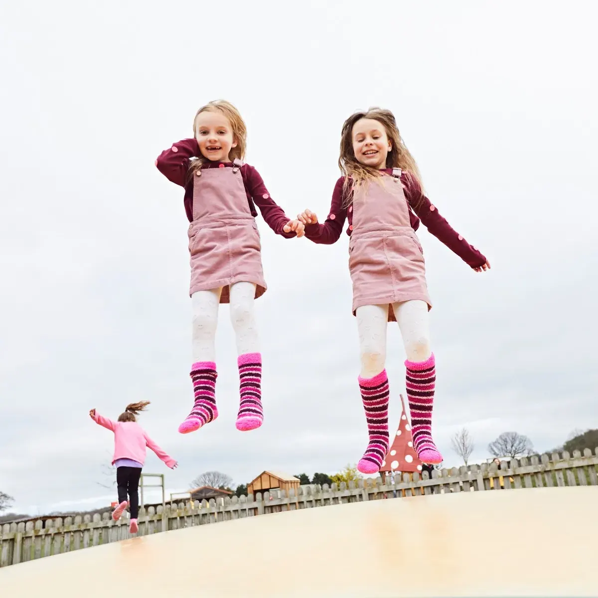 Three young children jumping and holding hands on a trampoline at a farm venue.