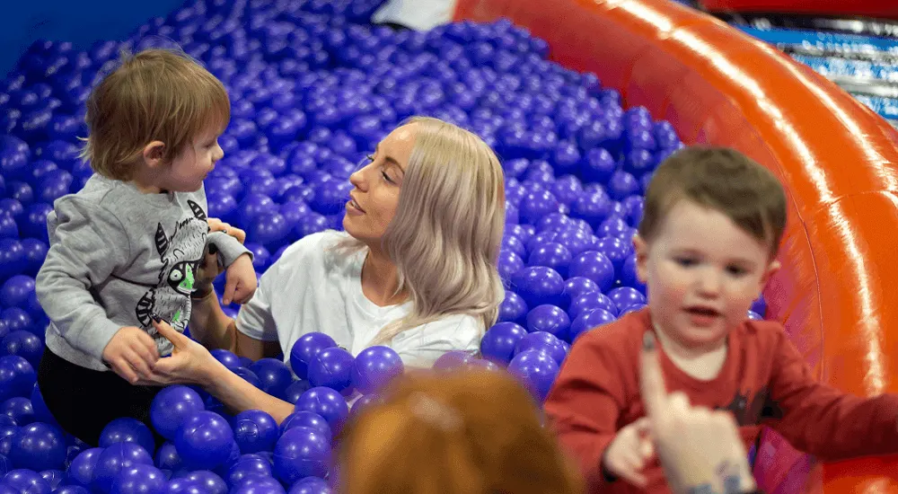 Adult and toddlers playing in a blue ball pit with an orange inflatable structure.
