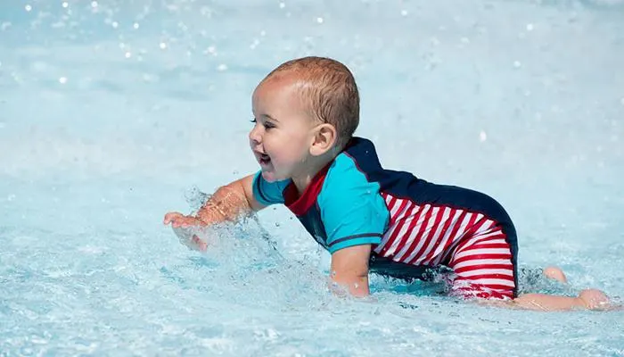 Young child in swim nappies and armbands playing in shallow pool water.