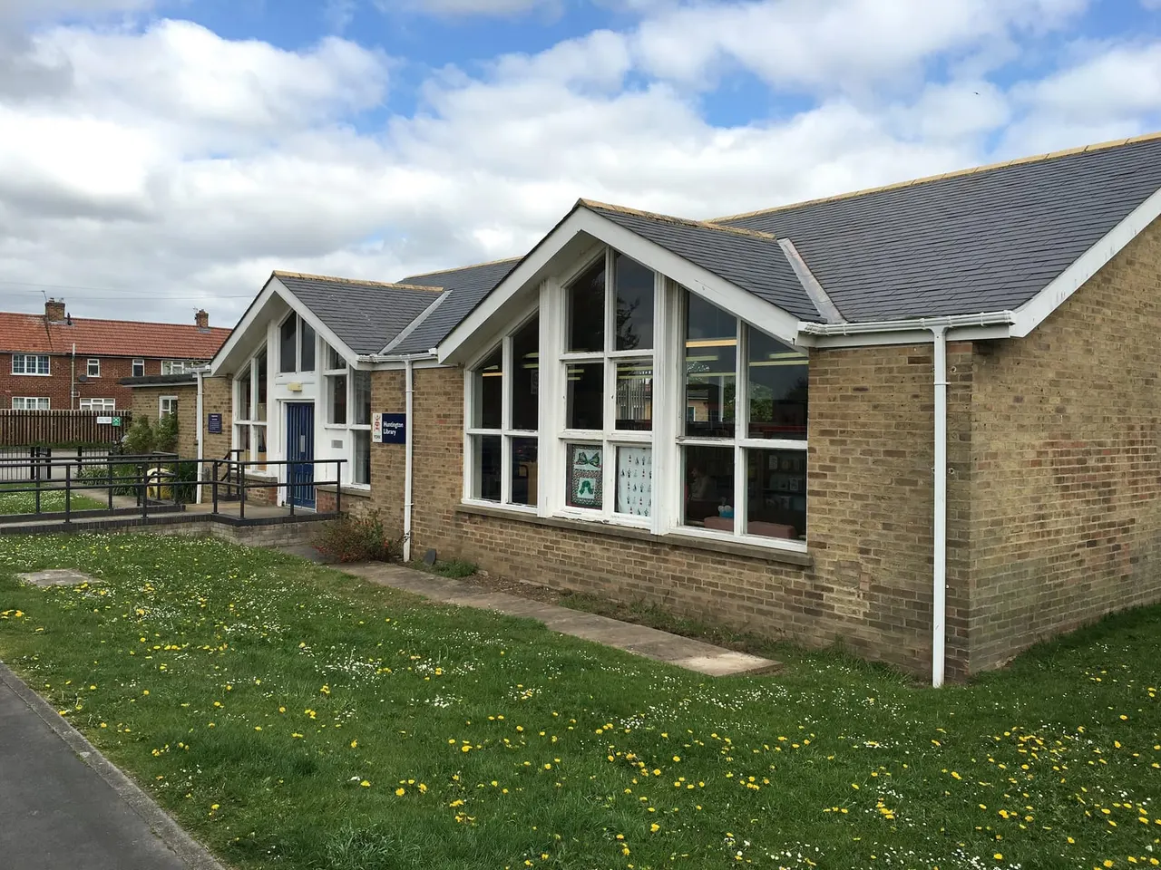 Modern brick building with large white-framed windows set in landscaped grounds with grass and yellow flowers.