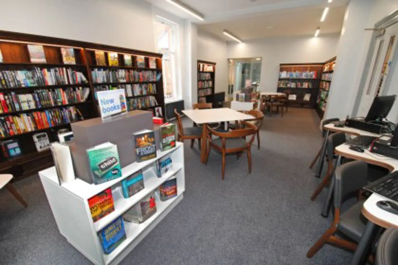 Library interior with bookshelves, computer workstations, display tables and seating areas.