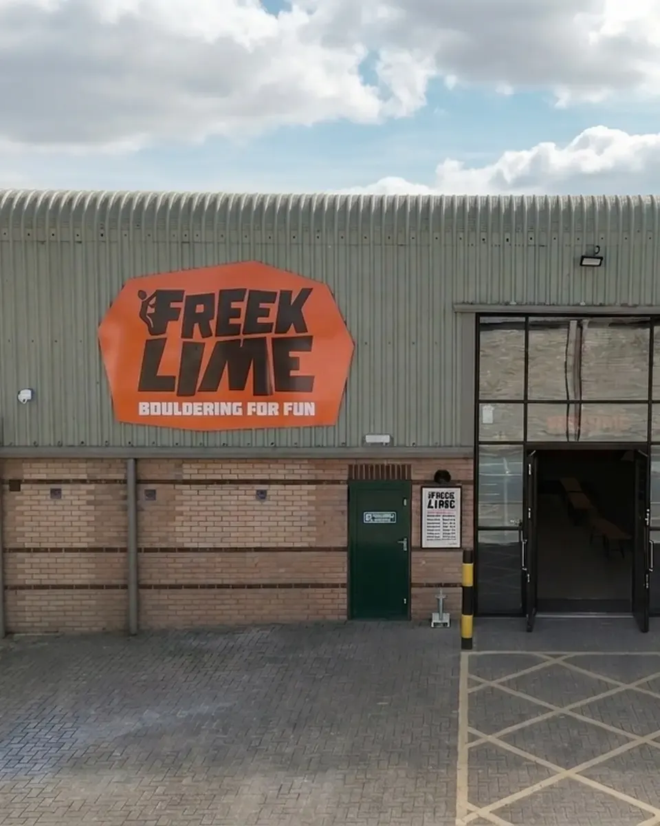Industrial building with orange sign reading "Freek Lime Bouldering for Fun" and entrance doors on brick and corrugated metal facade.