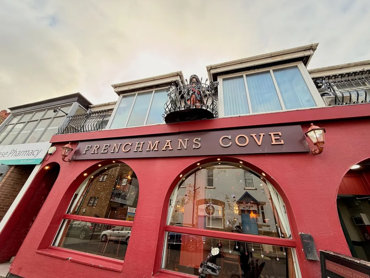Exterior of Frenchmans Cove leisure venue with bright red façade, large curved windows and ornamental ironwork above.