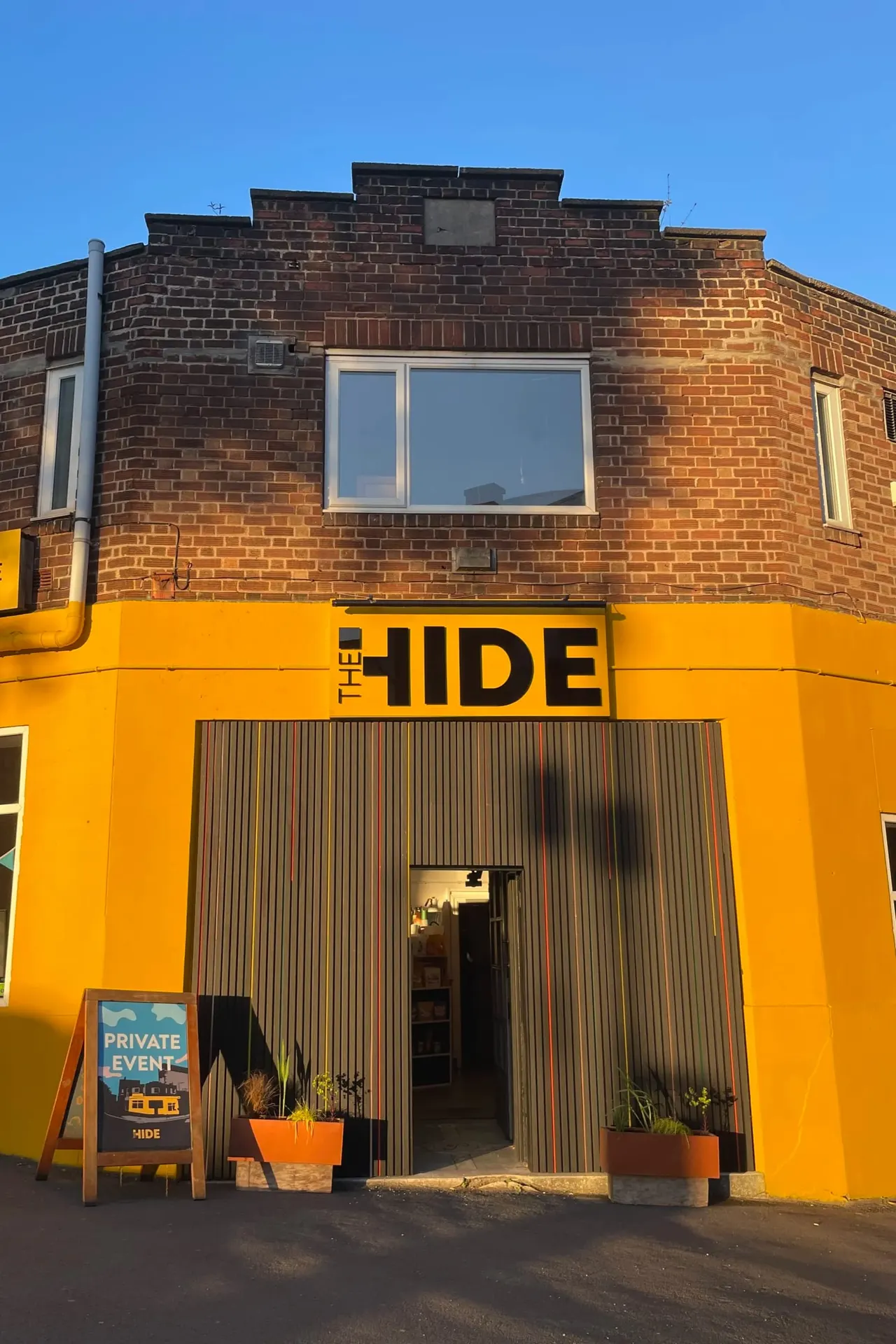 Bright yellow leisure venue building with corrugated metal entrance doors and brick upper storey against a clear blue sky.