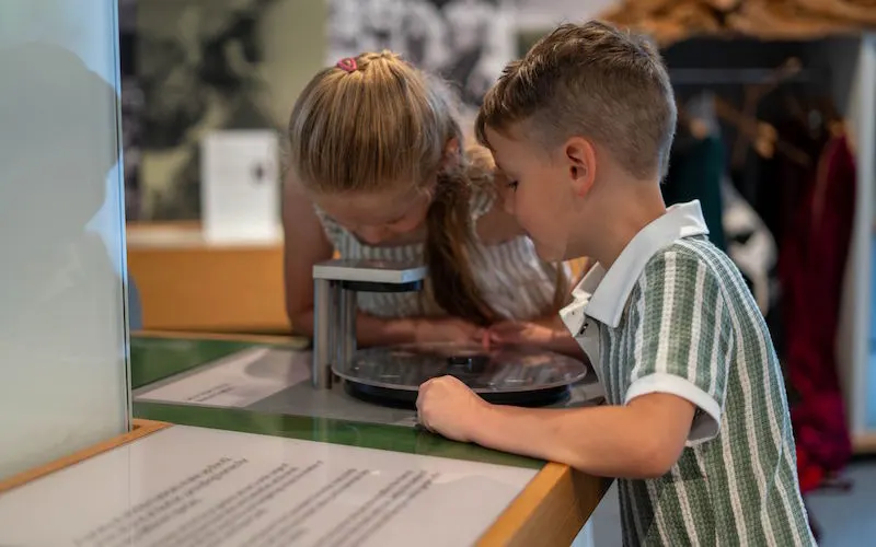 Two children interact with a touchscreen display at an indoor museum exhibit.