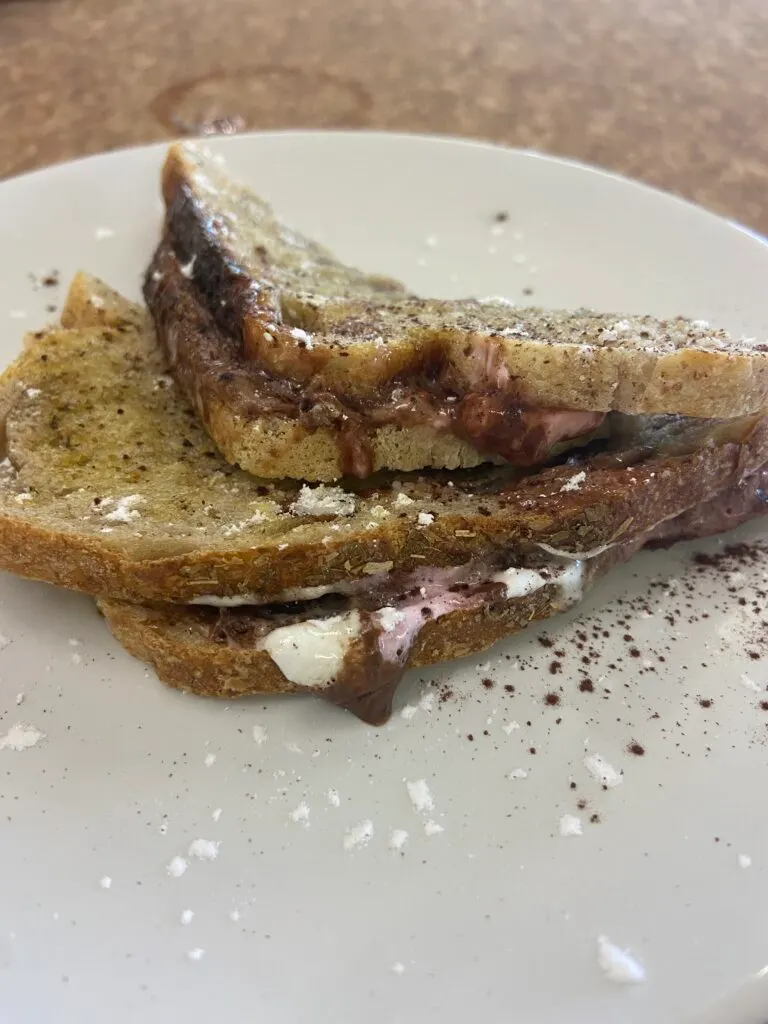 Toasted bread sandwich with meat filling and powdered sugar on a white plate.