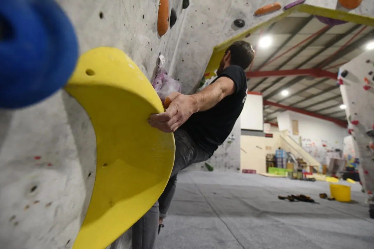 Person climbing an indoor rock wall with coloured handholds in a modern climbing gym.