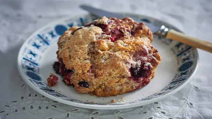 A fruit scone with red jam on a blue and white decorative plate with a fork.