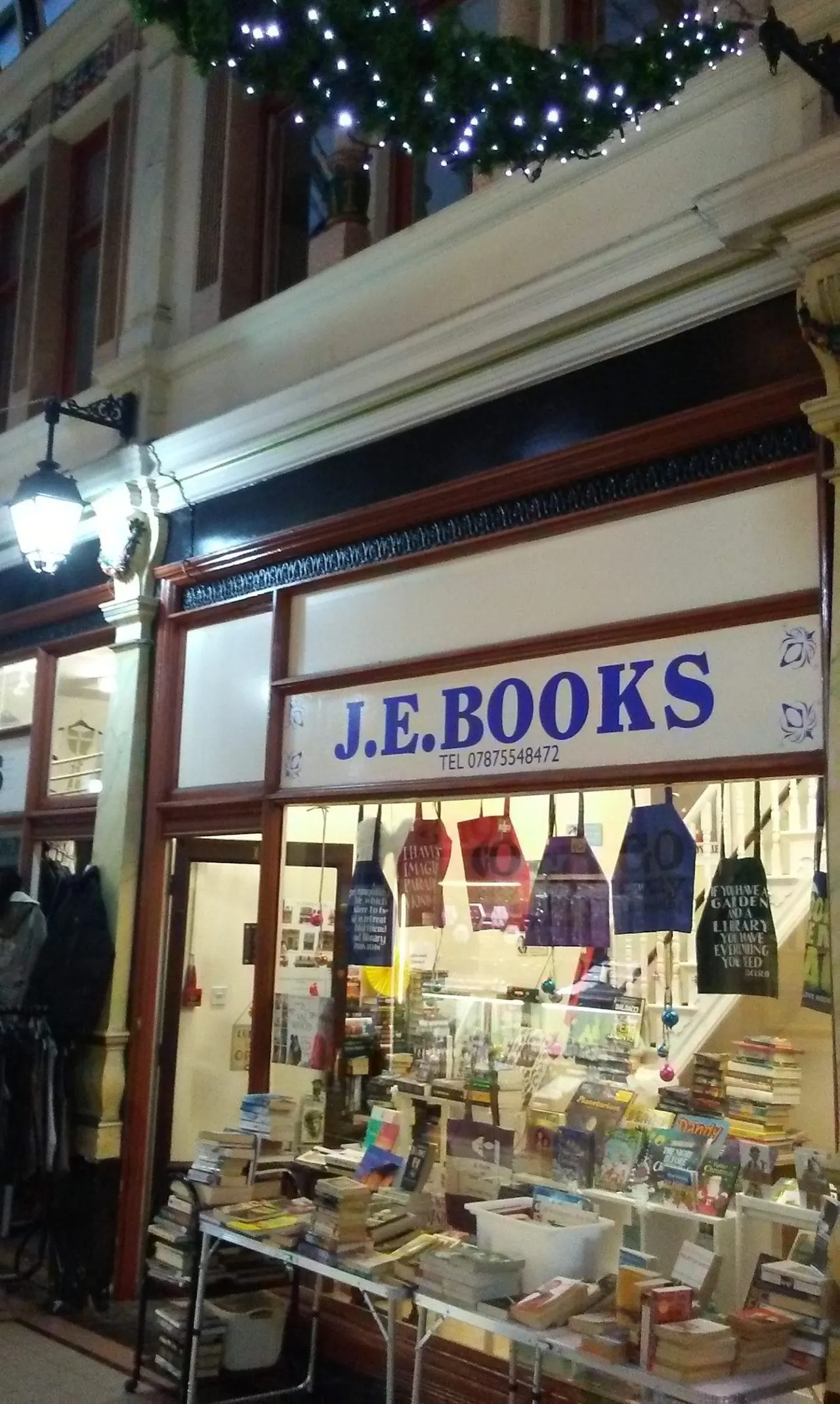 Illuminated bookshop storefront at night with Christmas garland and decorations hanging above.