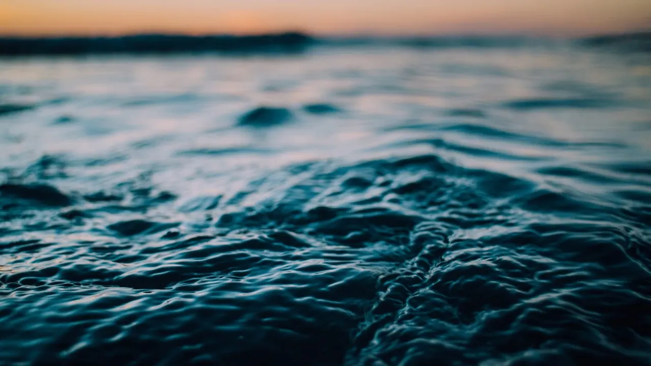 Ocean waves rolling onto shore at dusk, with shallow focus on foreground water.