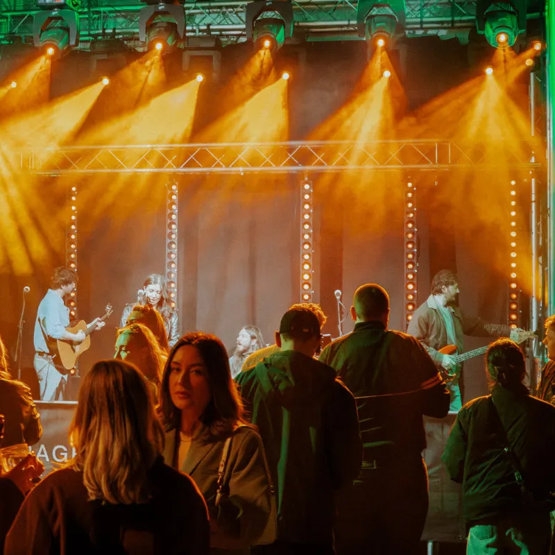 Crowd of people watching a live band perform on an illuminated stage with golden spotlights and decorative lighting.