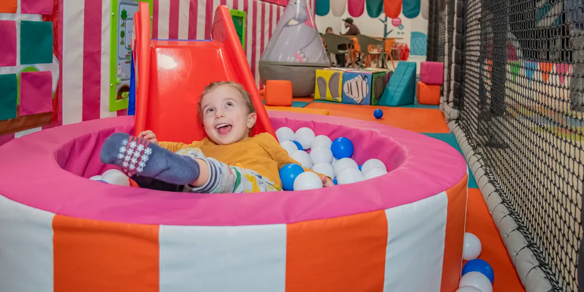 Young child playing in a colourful ball pit at an indoor soft play centre.