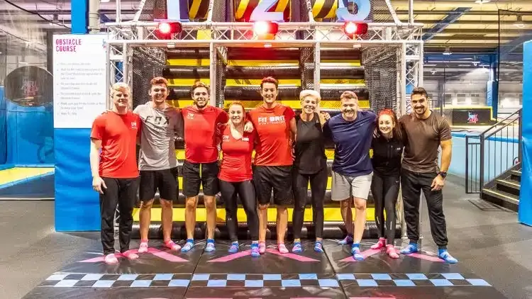 Group of ten people in casual and sports clothing posing together inside an indoor trampoline park with colourful equipment.