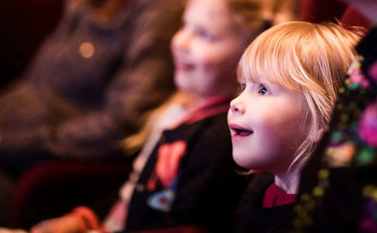 Young child with blonde hair gazing in wonder at a festive display with coloured lights.