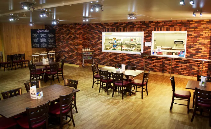 Interior of a casual dining restaurant with wooden tables, dark chairs, and exposed brick walls.