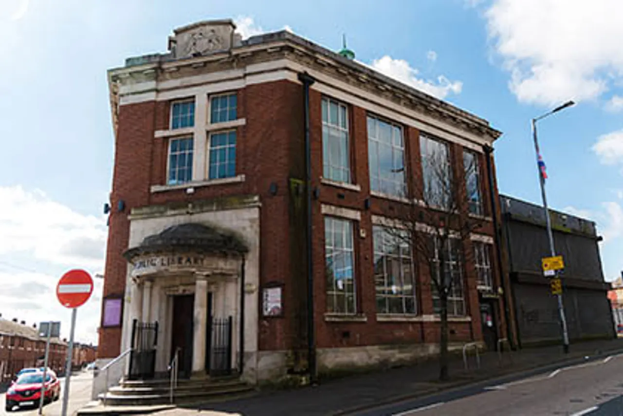 Historic red-brick library building with classical entrance portico and clock tower, situated on a residential street.