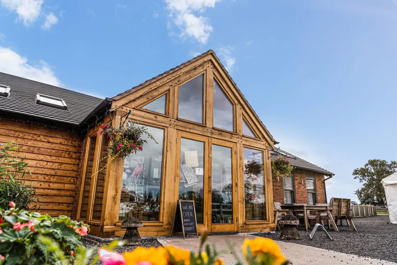 Wooden-framed glass extension on a brick farmhouse building with colourful hanging baskets and flowering plants in the garden.