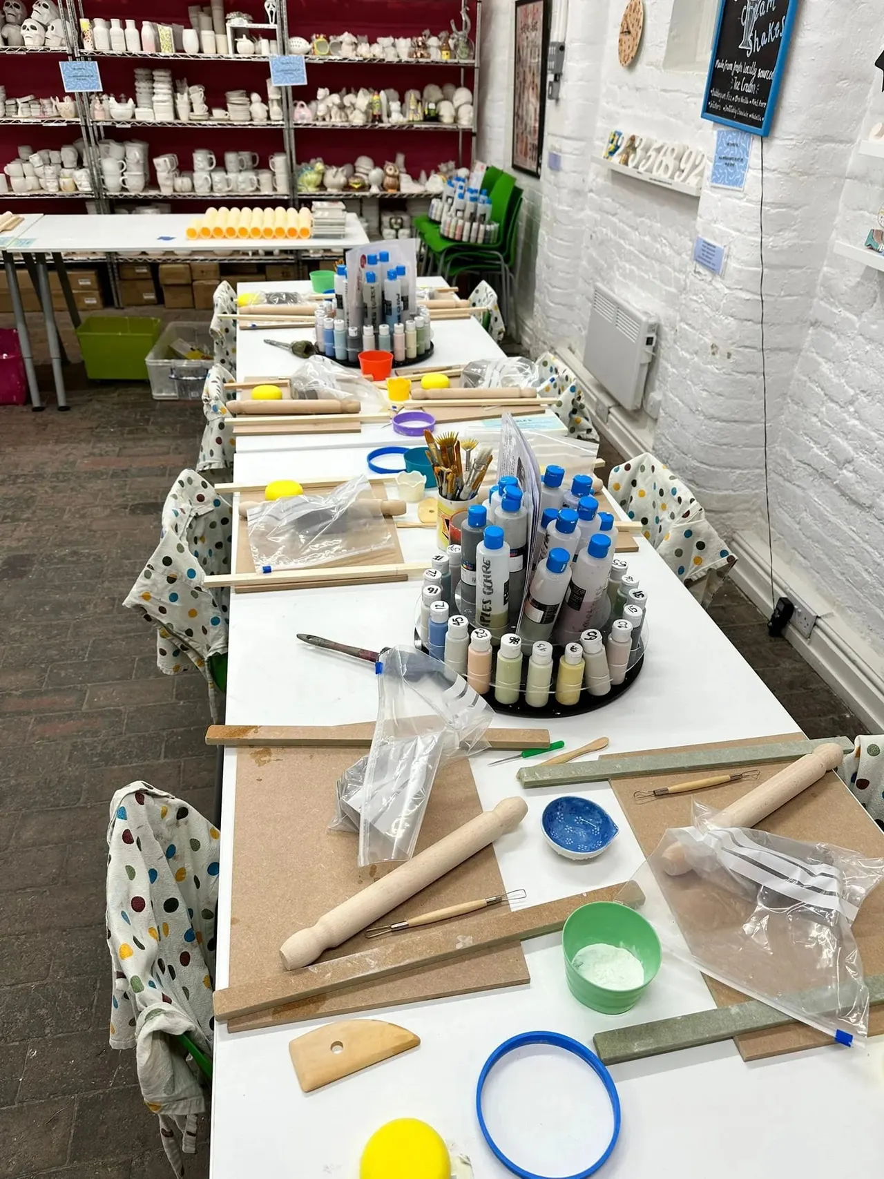 Multiple pottery painting workstations set up with paints, brushes, palettes and ceramic pieces ready for painting.