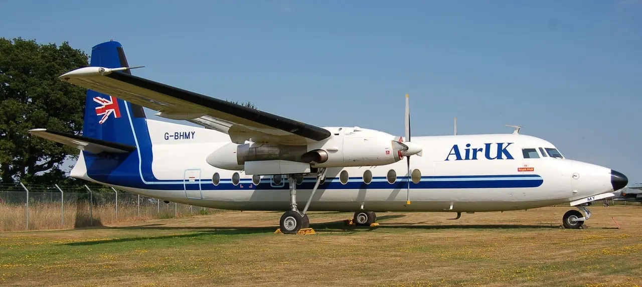 Retired Air UK turboprop airliner parked on grass at an aviation museum under clear blue sky.
