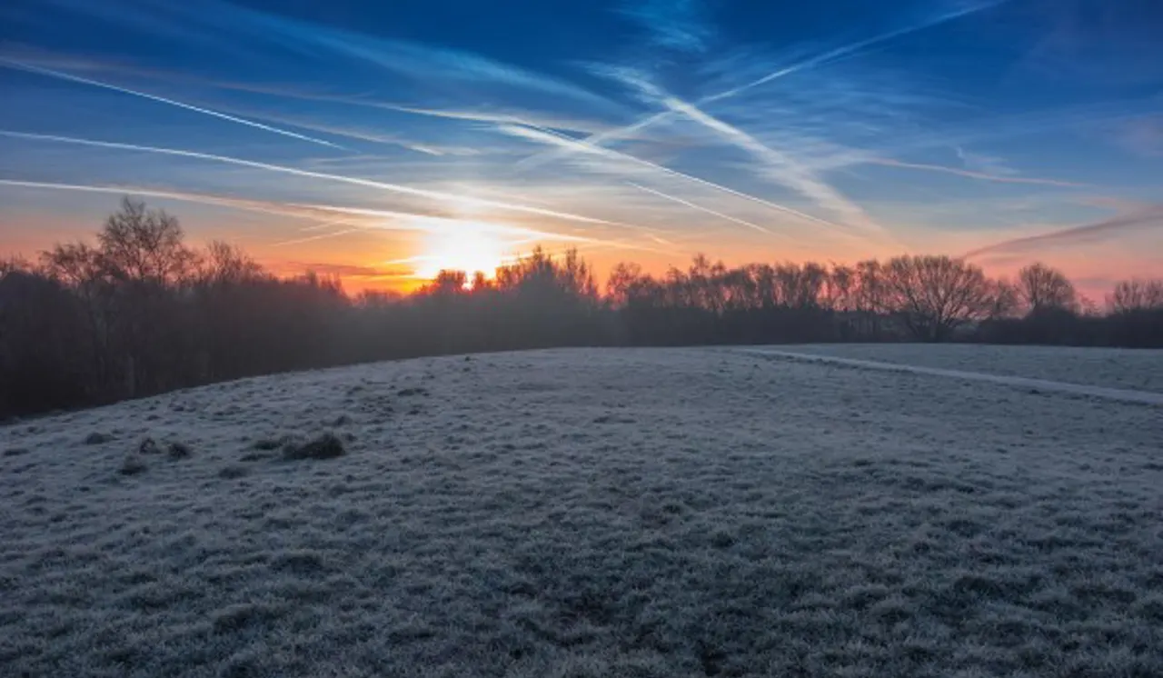 Frost-covered field at sunrise with bare trees lining the horizon beneath a blue and orange sky.